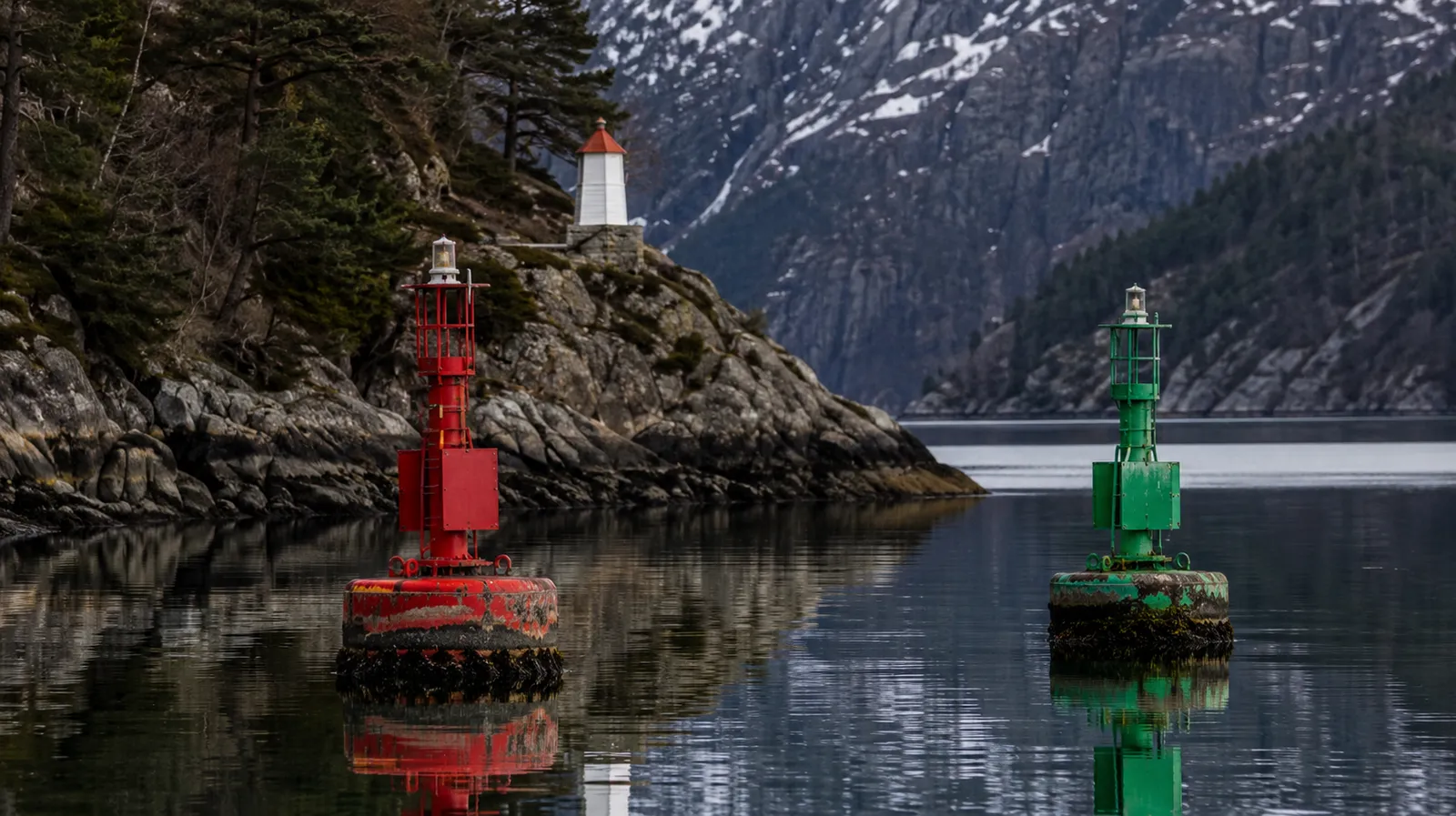 Rød og grønn lateral sjømerke-bøye i et trangt fjordløp med rolig vann.